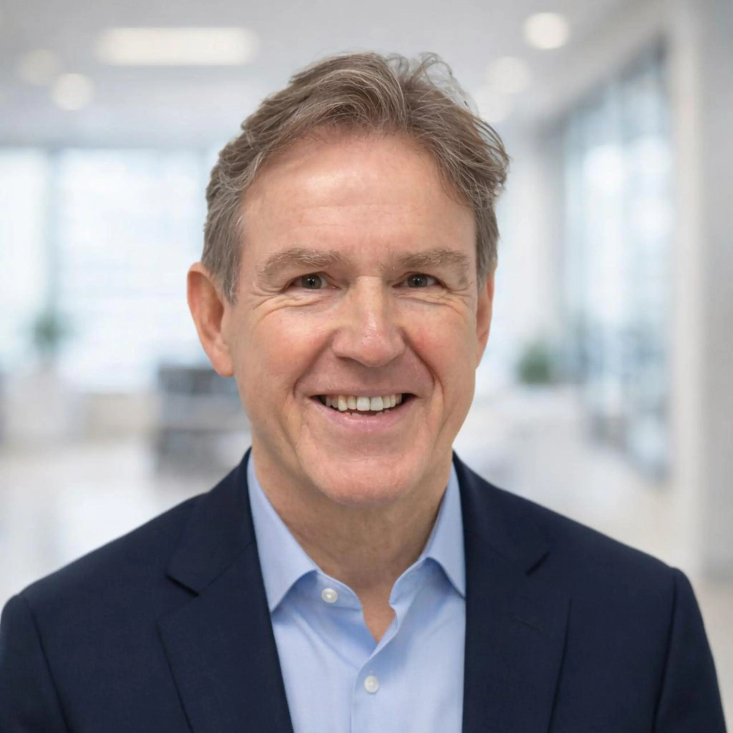 Dave Gibson smiling in a formal suit with a light blue shirt in a professional setting.